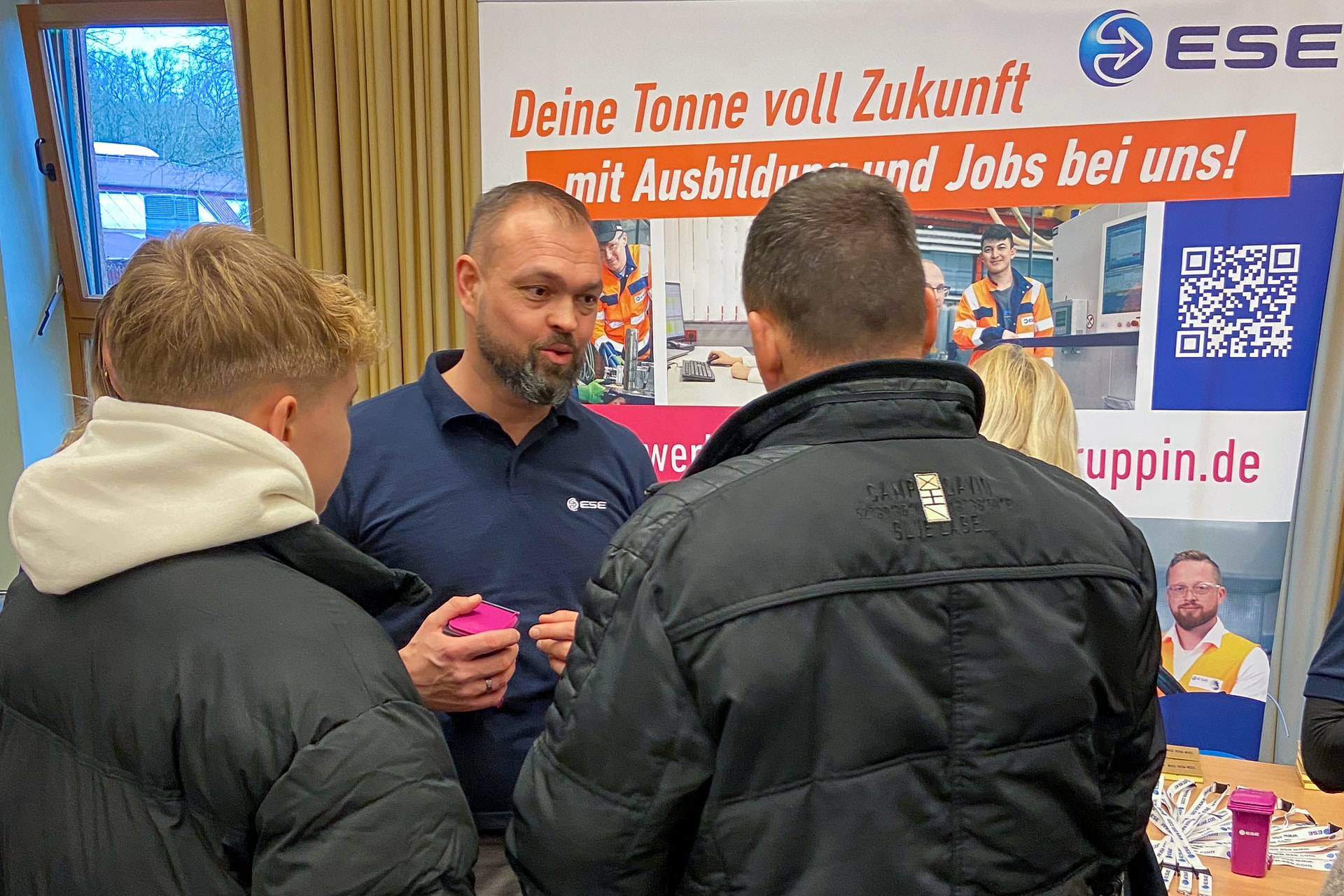 Stephan Schillkowski von ESE (Bildmitte) spricht mit zwei Besuchern am Infostand auf der Ausbildungsmesse 2025 im OSZ Neuruppin.