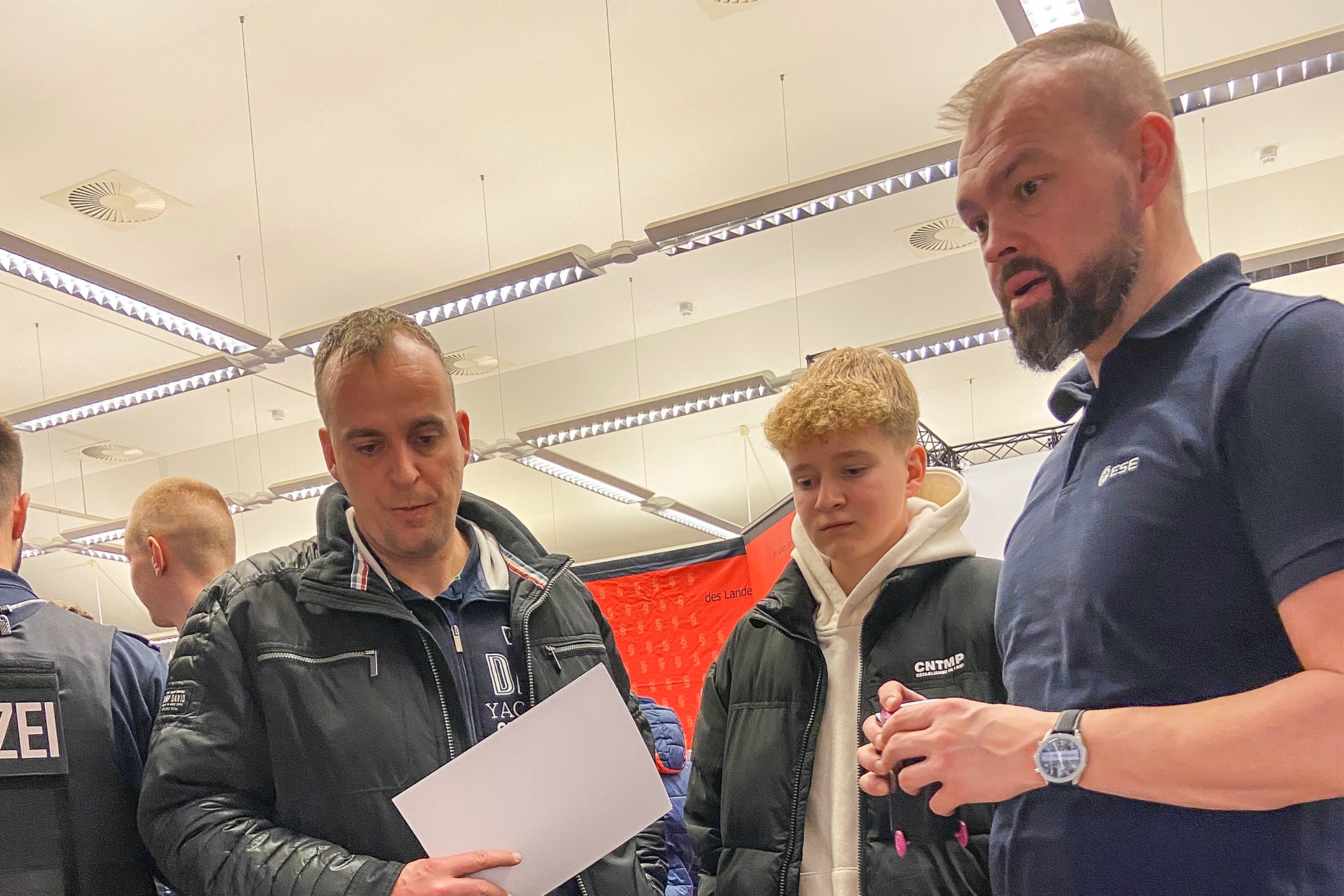 Stephan Schillkowski von ESE (Bildmitte) spricht mit zwei Besuchern am Infostand auf der Ausbildungsmesse 2025 im OSZ Neuruppin.